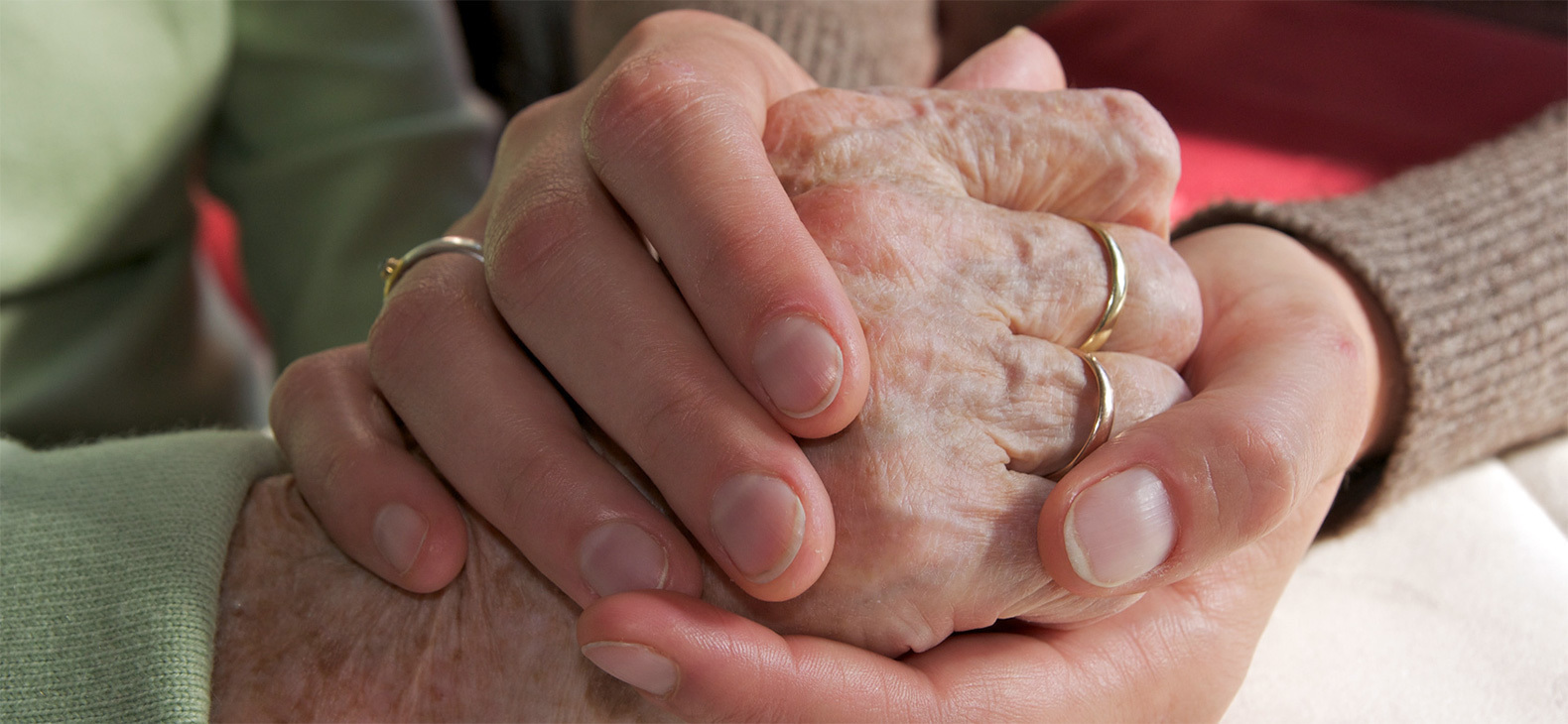 Die Hand einer alten Frau wird von 2 Händen umschlossen.