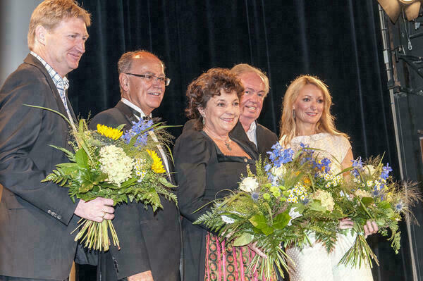 Gruppenfoto auf einer Bühne. Mit Ausnahme des Bezirkstagspräsidenten halten alle Blumensträuße in den Händen.