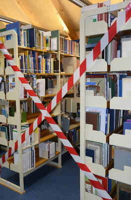 Zwei weiße Bücherregale gefüllt mit Büchern. Der Zugang ist gesperrt durch ein rot-weißes-Sperrband.
