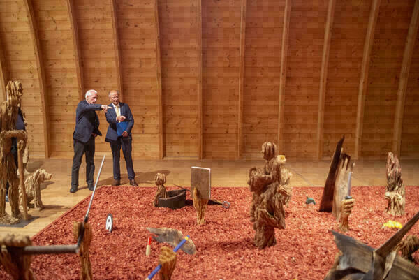 Panoramafoto der Ausstellungssituation im Tonnengewölbe von Schafhof - europäisches Künstlerhaus Oberbayern : Der Boden ist mit not gefärbten Holzstücken bedeckt. Auf diesen stehen viele Holzskulpturen, die mit der Kettensäge gestaltet wurden.
