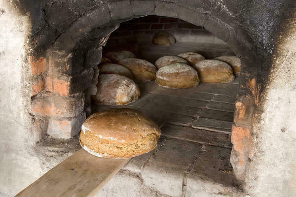 Gebackene Brote werden aus einem alten Ofen herausgeholt.