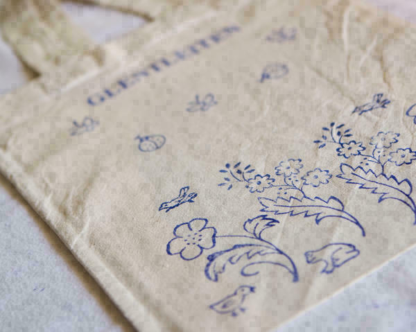 Detail einer wollweißen Stofftasche mit blauen Aufdrucken (Blumen, Käfer, Vögel).