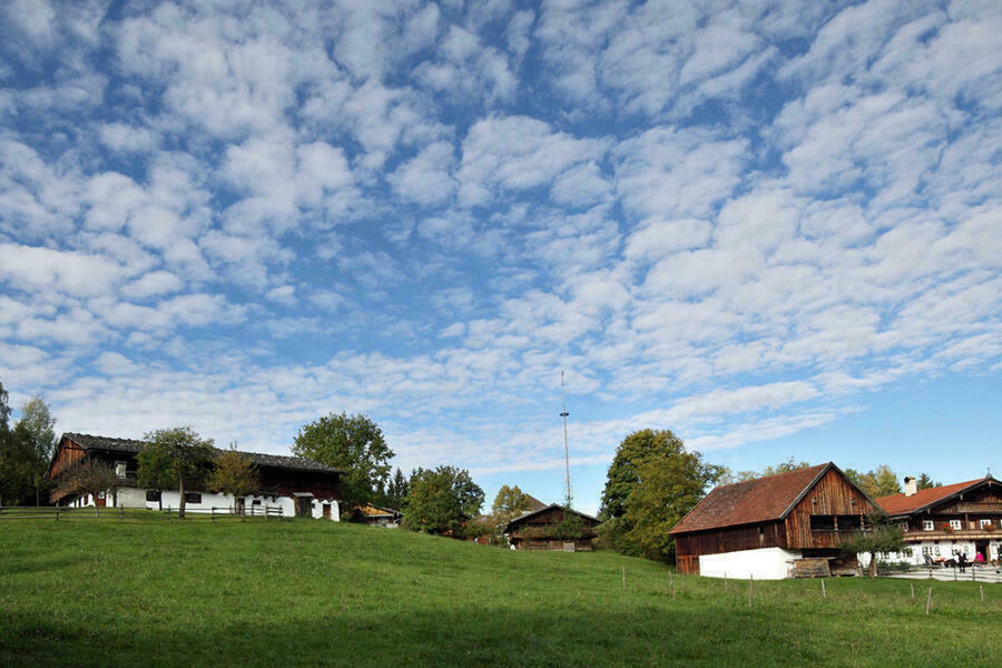 Historische Bauernhäuser unter leicht bewölktem Himmel, im Vordergrund grüne Wiesen.
