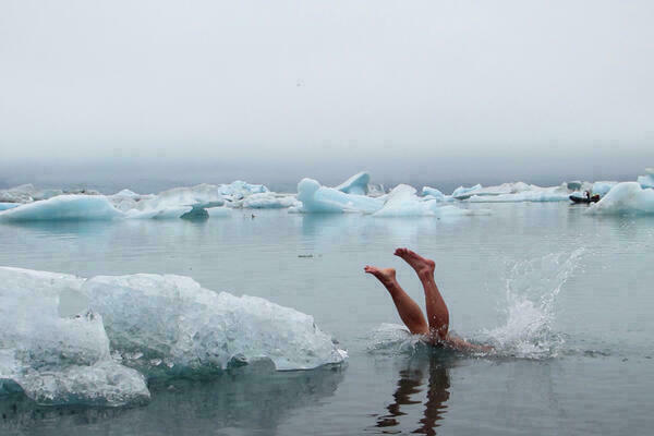 Ein Mensch springt in eiskaltes Wasser, es sind nur noch seine Beine zu sehen. Im Hintergrund schwimmen Eisschollen.
