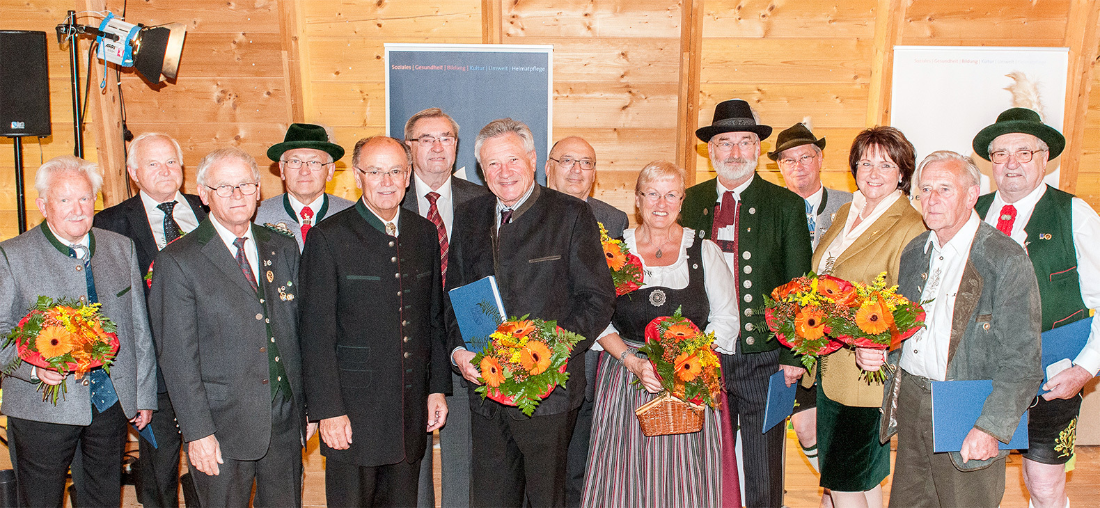 Gruppenfoto mit 13 Männer und Frauen die mit der Bezirksmedaille ausgezeichnet wurden; einige halten Blumensträuße in den Händen.