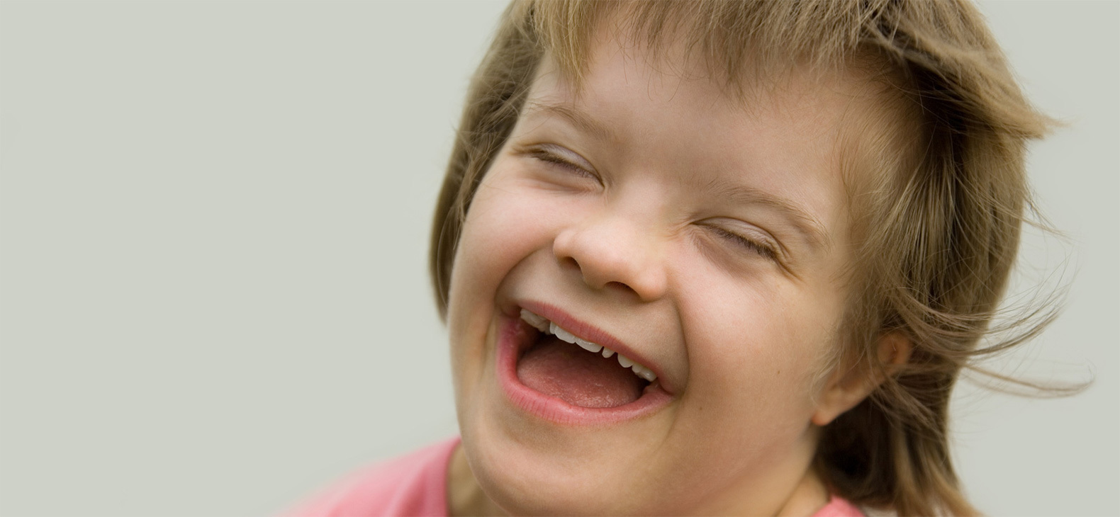 Ein junges Mädchen lacht mit geschlossenen Augen. Sie hält den Kopf dabei schräg