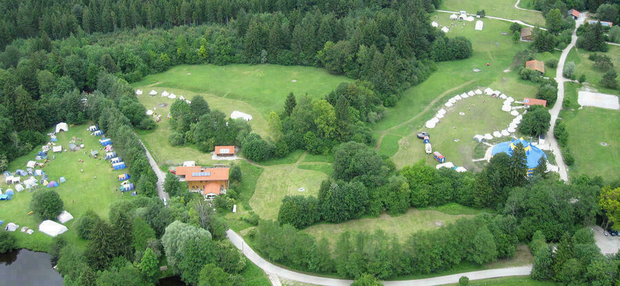Luftbild auf das Gelände der Jugendsiedlung Hochland mit Wald, Wiesen, Häusern und einem Zirkuszelt