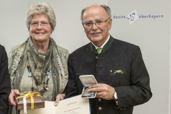 Preisträgerin und Bezirkstagspräsident halten lächelnd Urkunde und Medaille in die Kamera 
