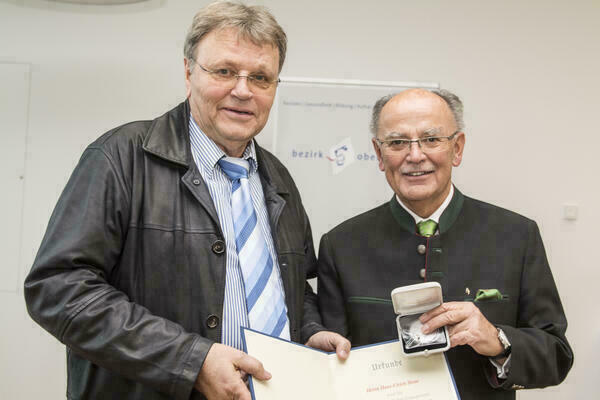 Preisträger und Bezirkstagspräsident halten lächelnd Urkunde und Medaille in die Kamera 
