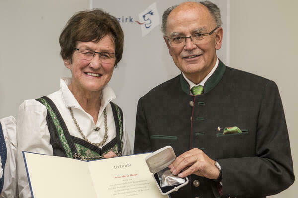 Preisträgerin und Bezirkstagspräsident halten lächelnd Urkunde und Medaille in die Kamera 

