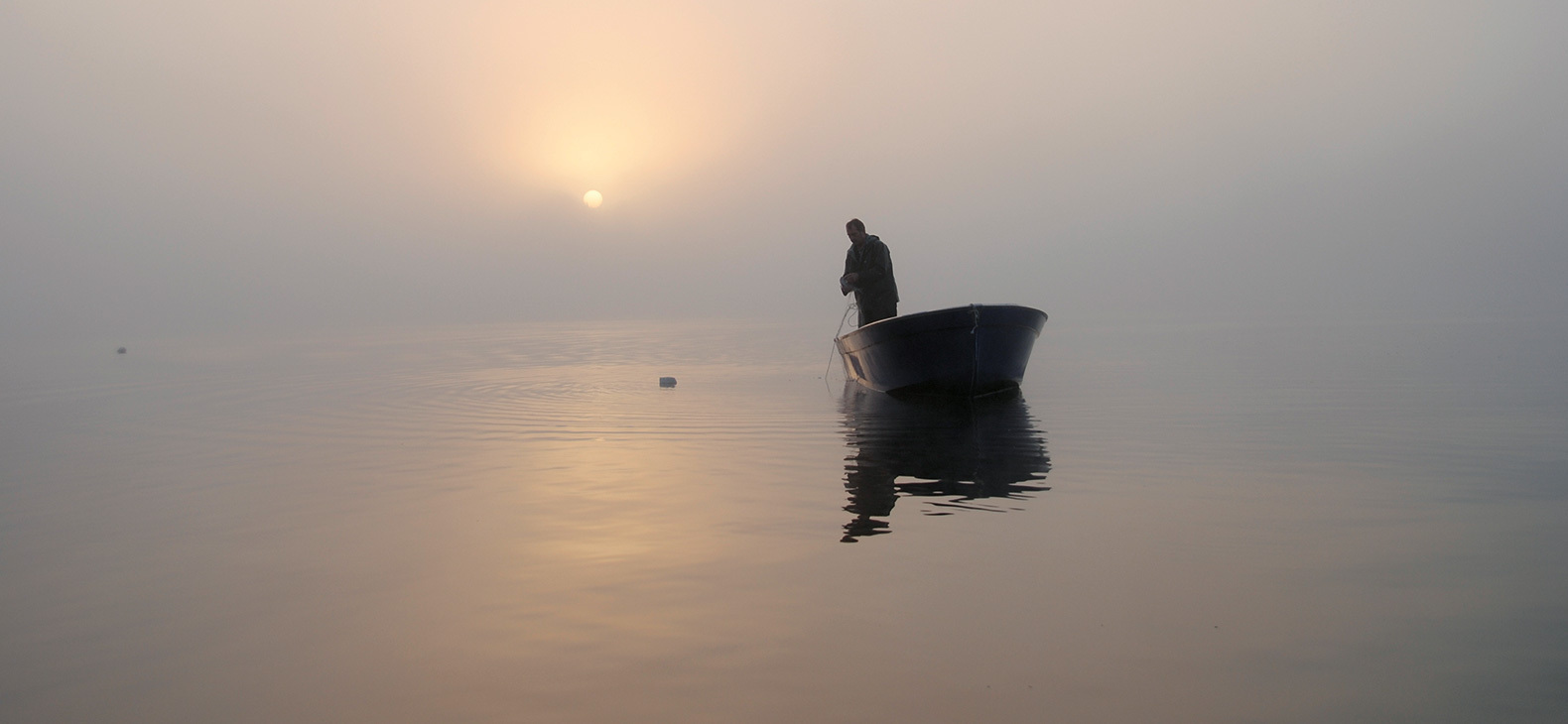 Mann in einem Boot auf einem See in der Morgendämmerung