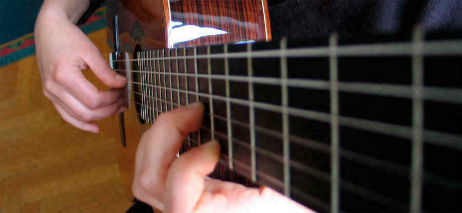 Foto entlang eines Gitarrenhalses nach unten: Eine Hand greift in die Saiten, die andere zupft sie.