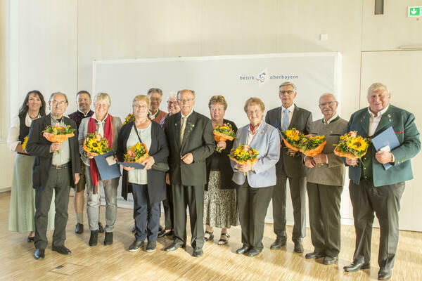 Gruppenfoto mit Männern und Frauen im Bezirk Oberbayern. Bis auf den Bezirkstagspräsidenten halten alle einen Blumenstrauß in der Hand.