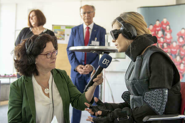 Eine Frau in einem dicken schwarzen Anzug mit Brille und Kopfhörern wird von einer anderen Frau interviewt