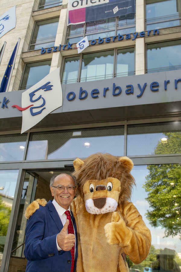Ein Mann und ein als Löwe verkleideter Mensch vor dem Eingang des Bezirks Oberbayern