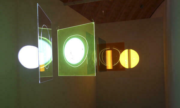 Eine frontal beleuchtete Installation, bestehend aus verschiedenen Glasscheiben, die durch ihre Positionierung Lichteffekte an den Wänden hinterlassen.