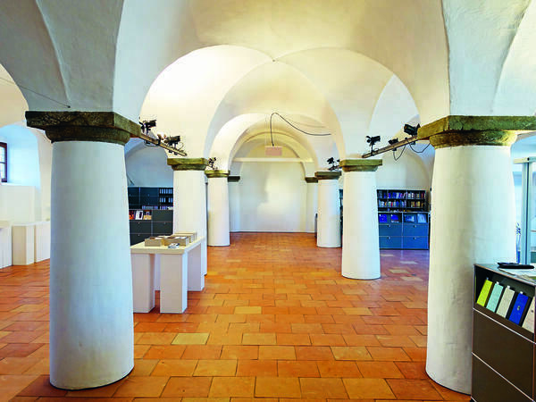 Ein heller, gewölbeartiger Raum mit einem zentralen Säulengang und gekacheltem Fussboden.
