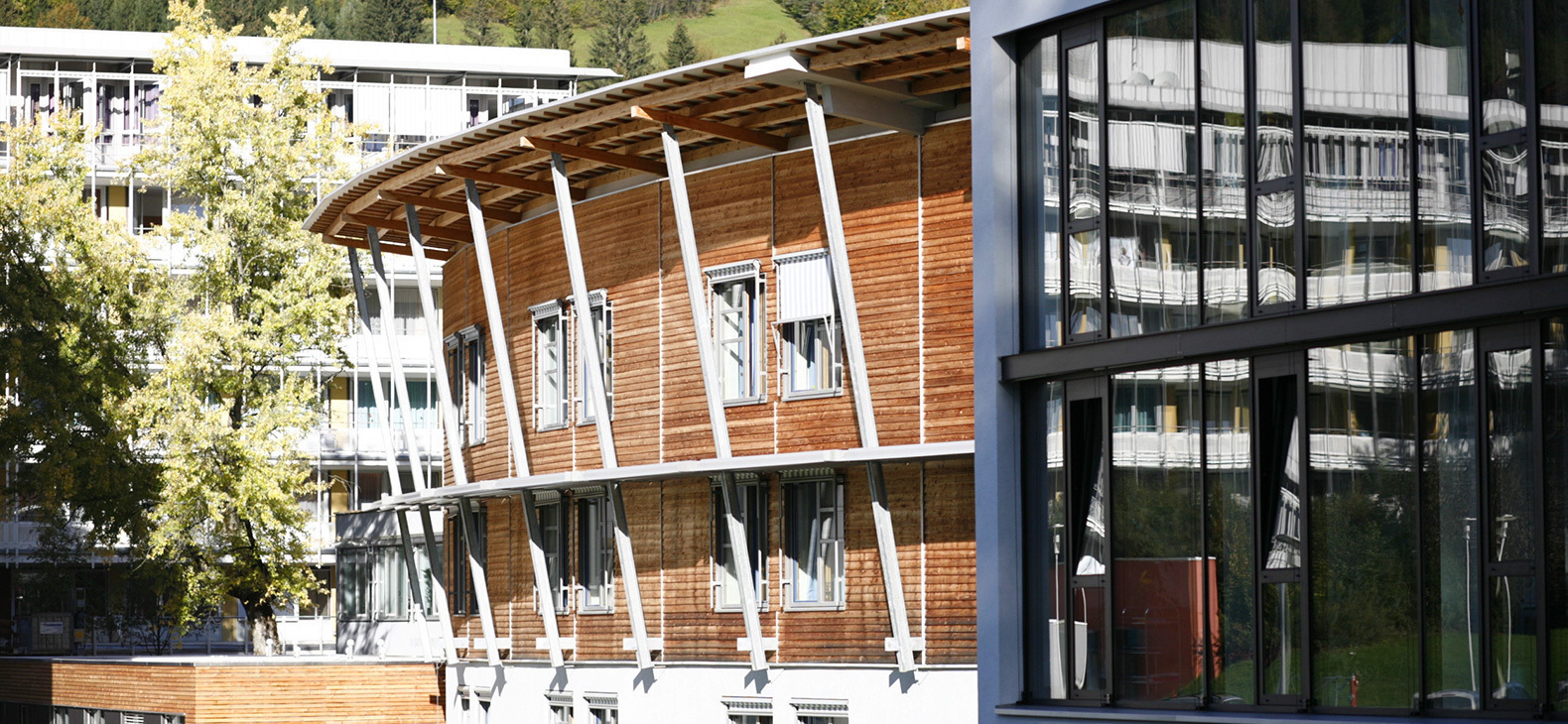 Außenfassade der kbo-Lech-Mangfall-Klinik in Garmisch-Partenkirchen: Blick auf einen Rundbau aus Holzelementen und weißen Stützen.