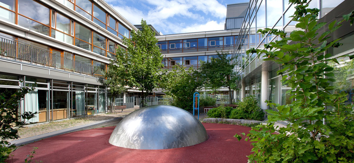 Innenhof der Carl-August-Heckscher-Schule mit Bäumen und einer halben Kugel in der Mitte