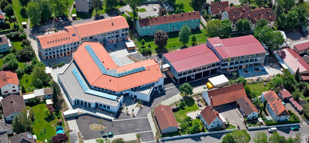Luftbild der Regens-Wagner-Berufsschule Schrobenhausen: zwei ältere Bauten und ein moderner L-förmiger Bau. Außenrum sieht man Wohnhäuser und Gärten.