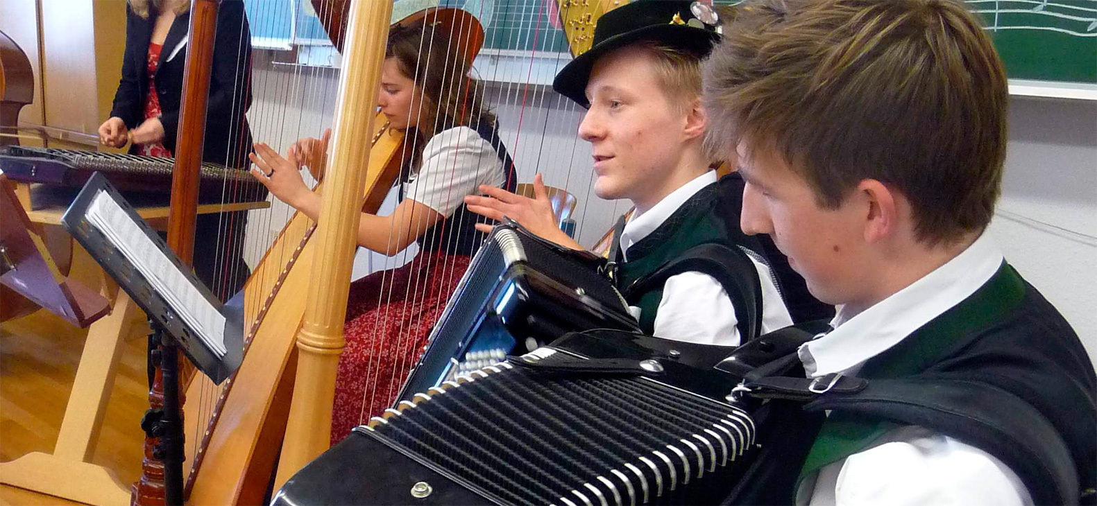 Junge Musikerinnen und Musiker in Tracht spielen in der Max-Keller-Schule in Altötting Ziehharmonika, Harfe und Hackbrett.