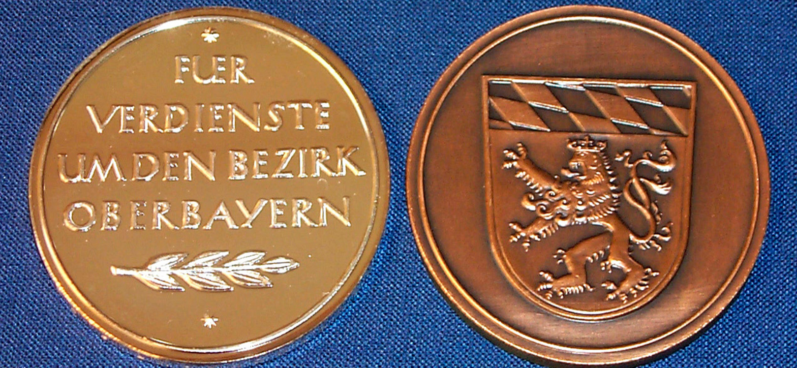 Beide Seiten der Medaille sind nebeneinander zu sehen; auf einer Seite steht der Text "Für Verdienste um Oberbayern", auf der anderen Seite ist das Wappen von Oberbayern eingraviert.