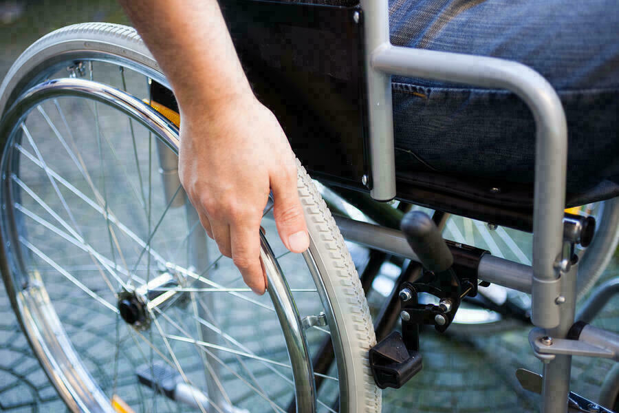 Bildausschnitt mit der Hand eines Mannes am Rad seines Rollstuhls.