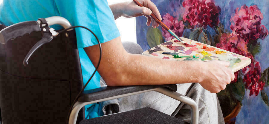 Person im Rollstuhl malt ein Bild auf einer Leinwand