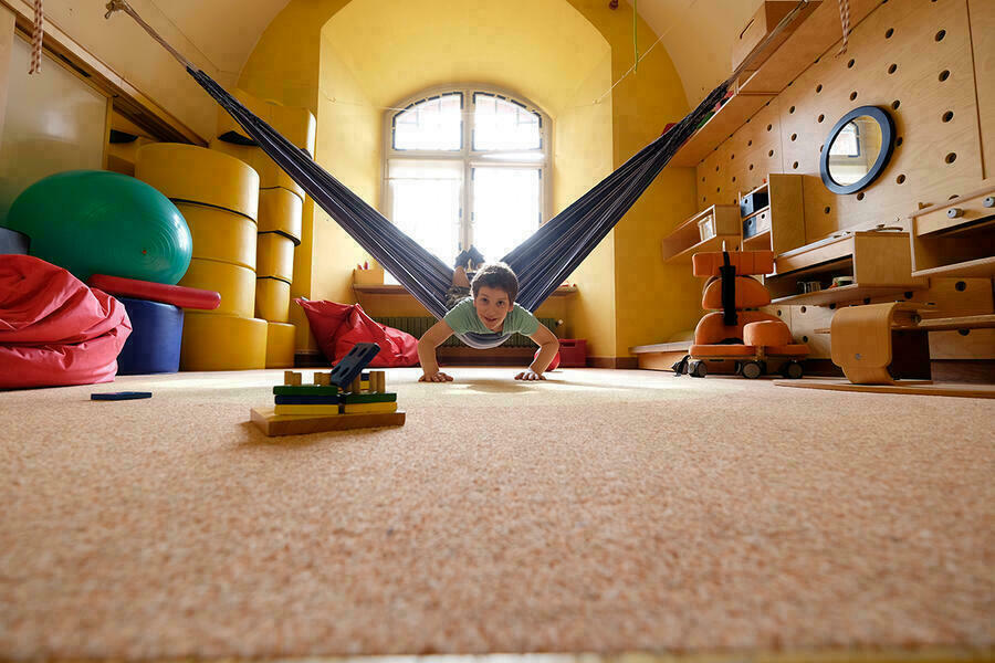 Bei einer Therapiestunde in der Kurz-Schule in Ingolstadt für Kinder mit körperlichen und motorischen Einschränkungen liegt ein Junge liegt auf dem Bauch in einer Hängematte und stützt sich am Boden mit den Händen ab.