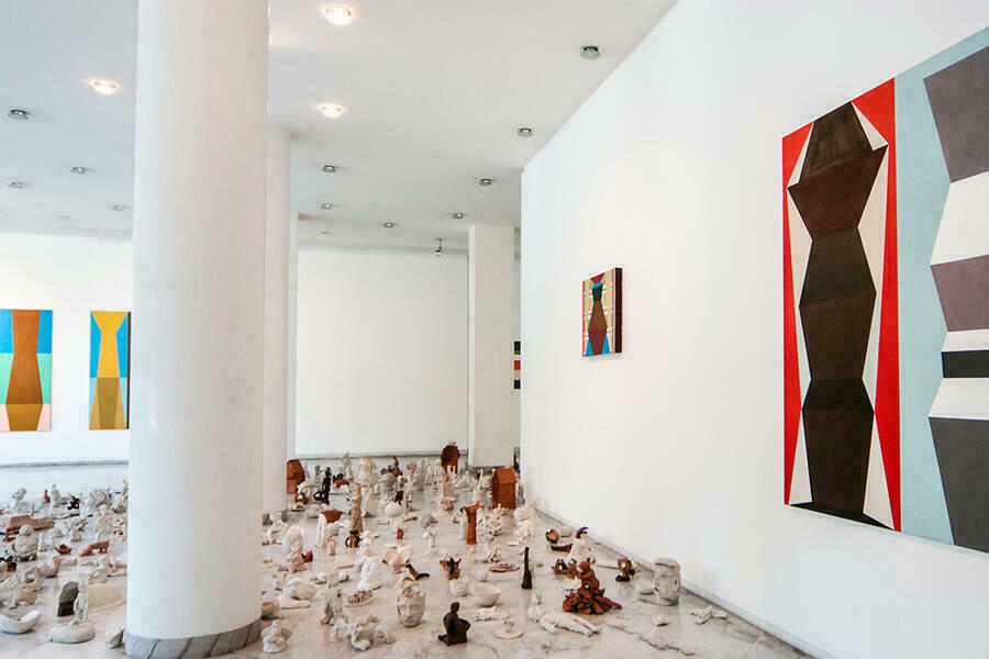 Blick in eine Ausstellung in der Galerie des Bezirks Oberbayern. An den Wänden abstrakte Bilder am Boden der galeire kleine Skultprue aus Ton