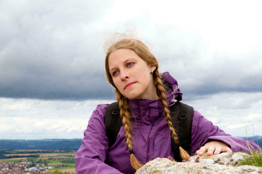 Junge Frau mit 2 geflochtenen Zöpfen vor offener Landschaft mit Bergen.