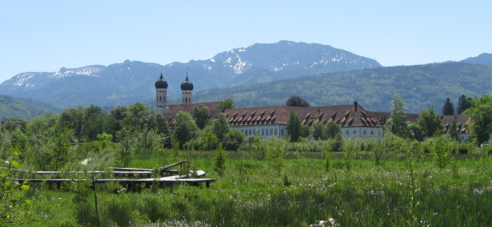 Das Erlebnisbiotop des Zentrums für Umwelt und Kultur Benediktbeuern mit seinem Sitz, dem Kloster Bendiktbeuern und den Bergen im Hintergrund.