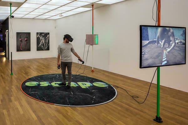 Ein Mann mit einem VR-Headset steht mitten in einem Raum auf einer großen runden Fußmatte mit dem Schrifftzug 