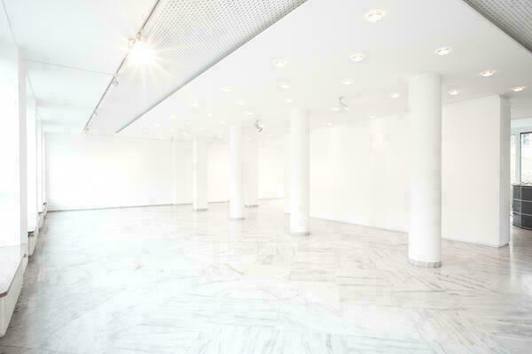 Ein leerer, weißer, langezogener Raum in einer Galerie, in dem mehrere Säulen und ein Pfeiler vor einer mittigen Trennwand zu sehen sind