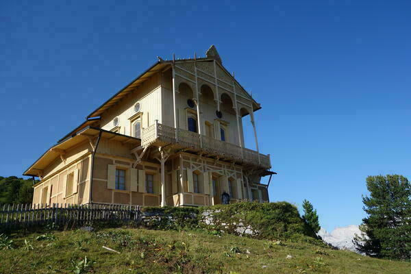 Blick auf ein großes Holzhaus mit verzierten Holzbalkonen auf einem Berggipfel