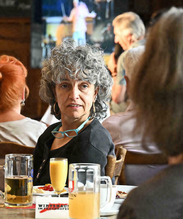 Foto von einer Frau, die in einer Gastwirtschaft sitzt. Sie schaut über den Tisch zu einer Gesprächsperson im Vordergrund.