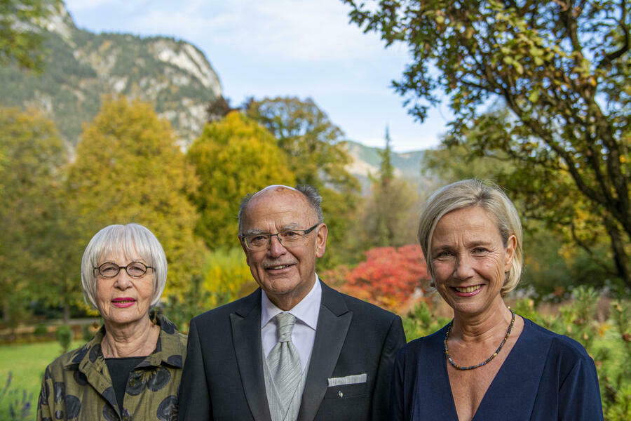 Gruppenfoto mit drei Erwachsenen vor einem Hintergrund aus Bäumen und Bergen
