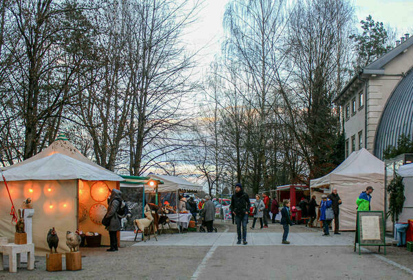 Ein Weihnachtsmarkt unter freiem Himmel mit Ständen links und rechts, in der Mitte laufen Menschen