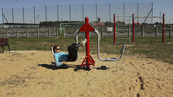 Foto: Eine Frau übt liegend auf einem Fitnessgerät. Im Hintergrund sieht man Zäune.