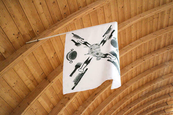 Im Tonnengwölbe des Schafhofs ist eine Fahne befestigt. Auf weißem Grund sieht man mehrere mit schwarzer Farbe gemalte Werkzeuge.