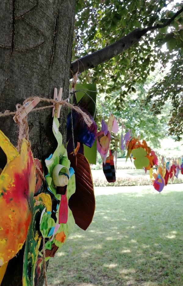 Verschiedene bunte Objekte hängen an einer zwischen Bäumen aufgespannten Wäscheleine. 