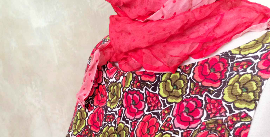 Im Bild ist ein Ausschnitt eines roten Kleids mit Blumenmuster an einer Schaufensterpuppe zu sehen.