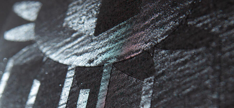 Ausschnitt aus Fotografie eines der Werke des ungarischen Künstlers Ádám Varga. Zu sehen ist eine Detaillaufnahme einer schwarzen Leinwand in die gezielt Muster hineingefräst wurden. Unter Lichteinstrahlung kommt ein Motiv zum Vorschein. Werk 04-17 aus der Reihe "Engraved Canvases".