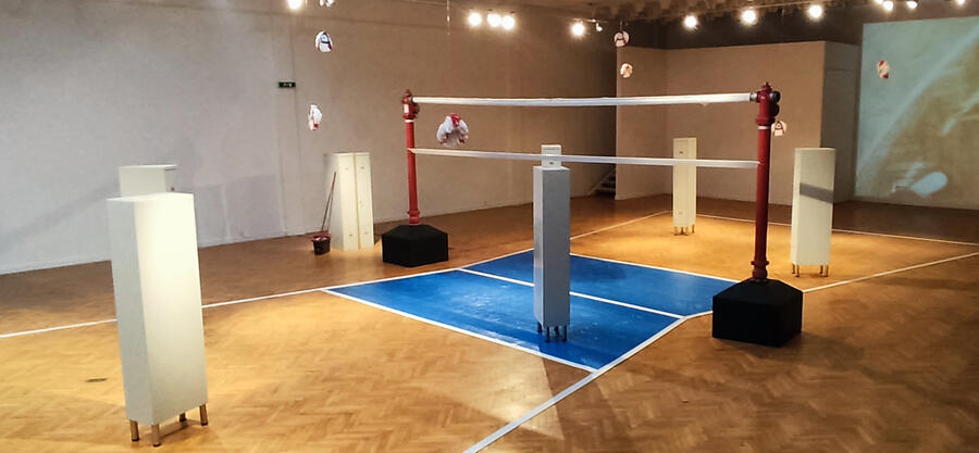 Remix: Im Bild ist ein Volleyballfeld zusehen. Im Raum verteilt sind mehrere weiße Schränke aufgestellt.