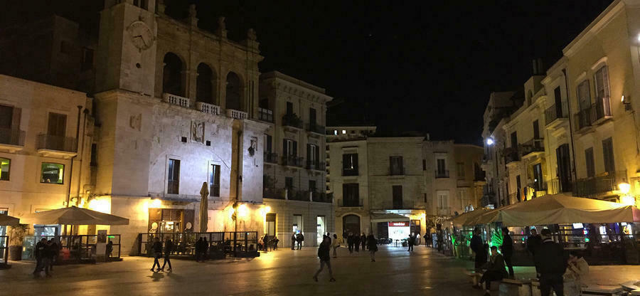 Aufnahme bei Nacht von einer Innenstadt. Auf der Straße laufen Menschen
