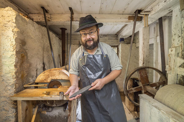 Ein Mann in Arbeitskleidung in einer Werkstatt hält einen Wetzstein in der Hand