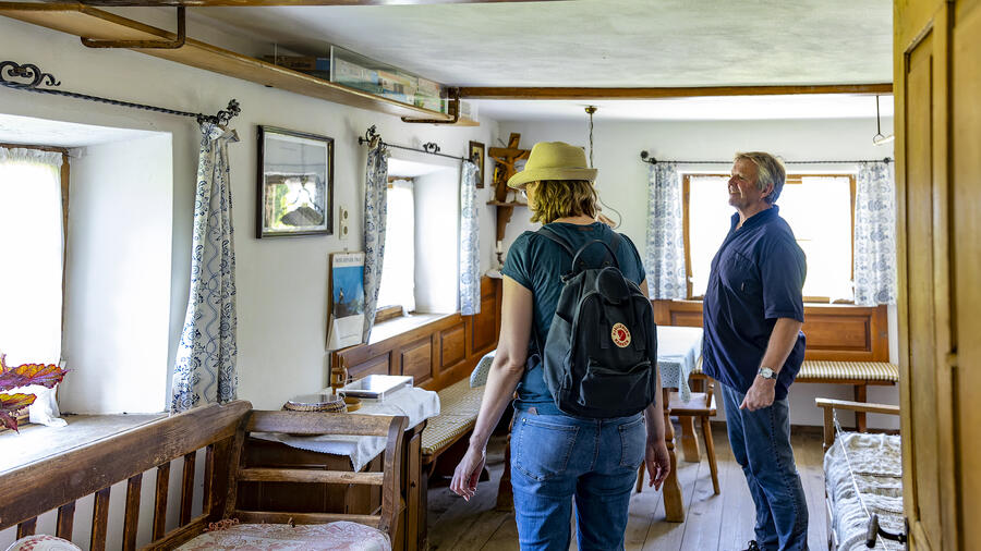 Ein Mann und eine Frau stehen in einem Wohnraum, der mit vielen Möbeln aus Holz eingerichtet ist.
