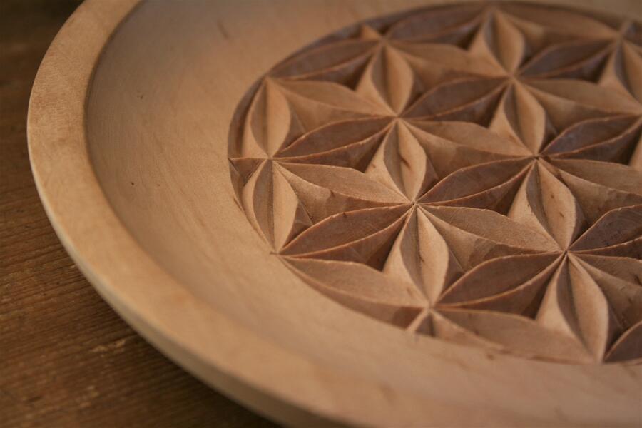 Ausschnitt einer Art runden Teller aus Holz, in den blumenförmige Ornamente geschnitzt wurden.