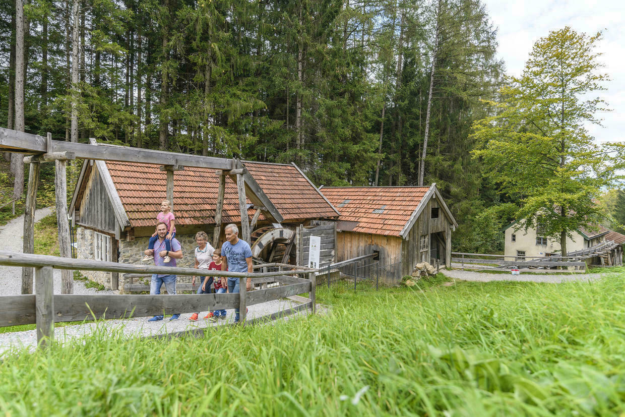 Eine Familie geht auf einem Weg, im Hintergrund eine Mühle mit Wasserrad.