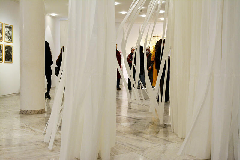 Ein Korridor aus weißen Papierstreifen verdeckt mehrere Besucher einer Ausstellung.